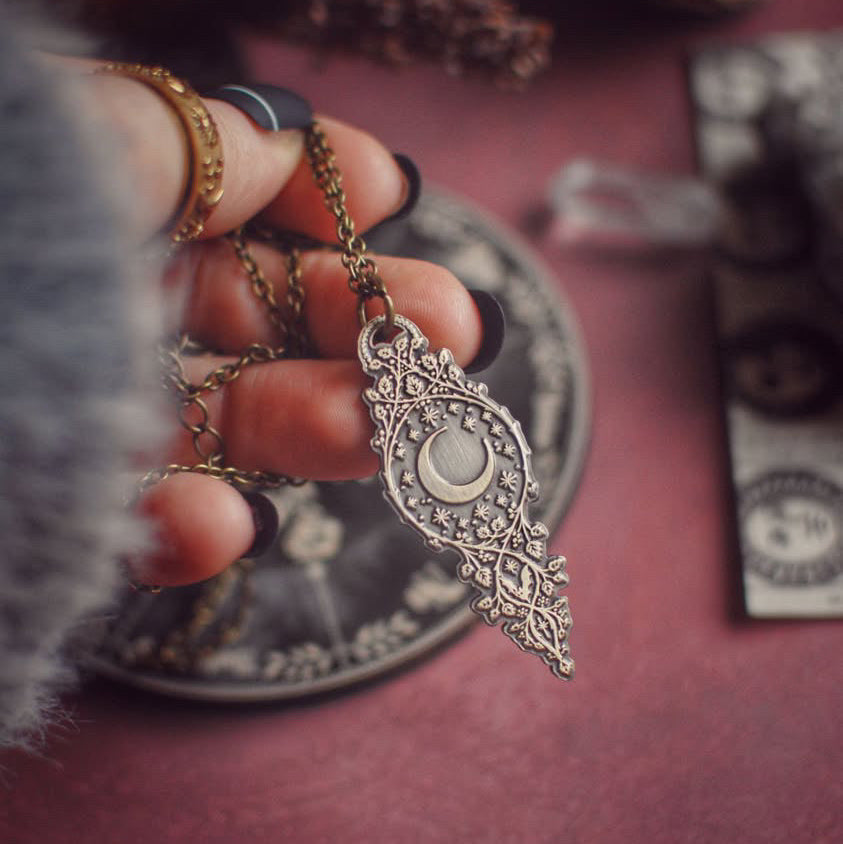 Hand holding a decorative pendulum with intricate designs on a red surface.