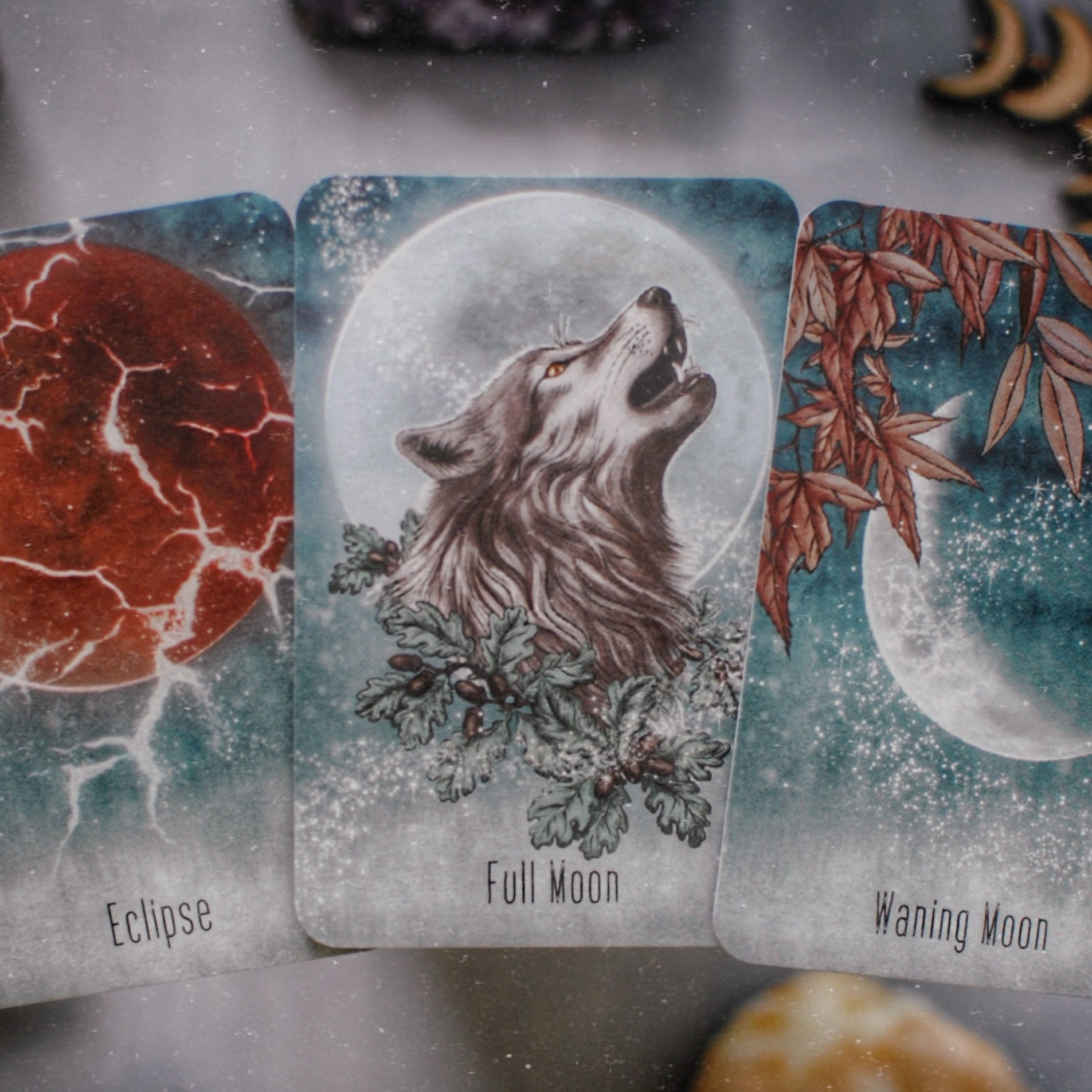 Three tarot cards titled 'Eclipse', 'Full Moon', and 'Waning Moon' on a textured surface with natural elements.