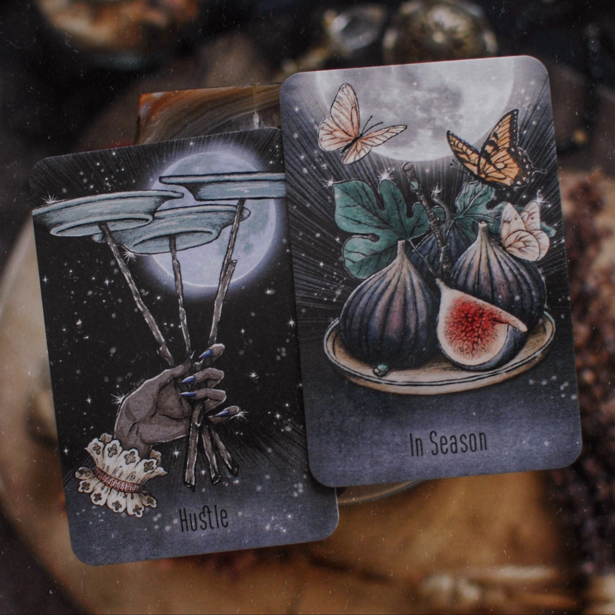 Two tarot cards with illustrations of a hand holding sticks and figs, set against a dark background.